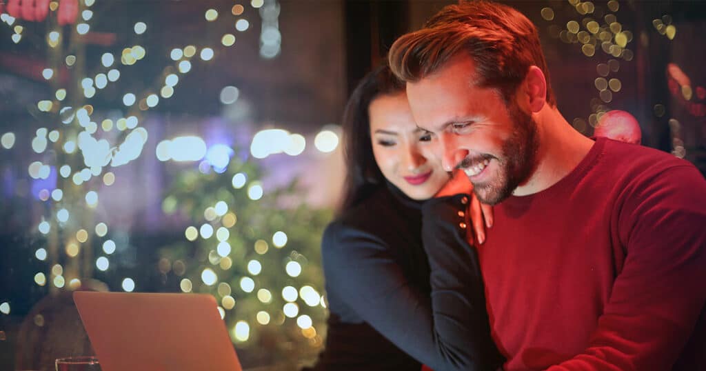 A man and woman smiling while looking at their PC