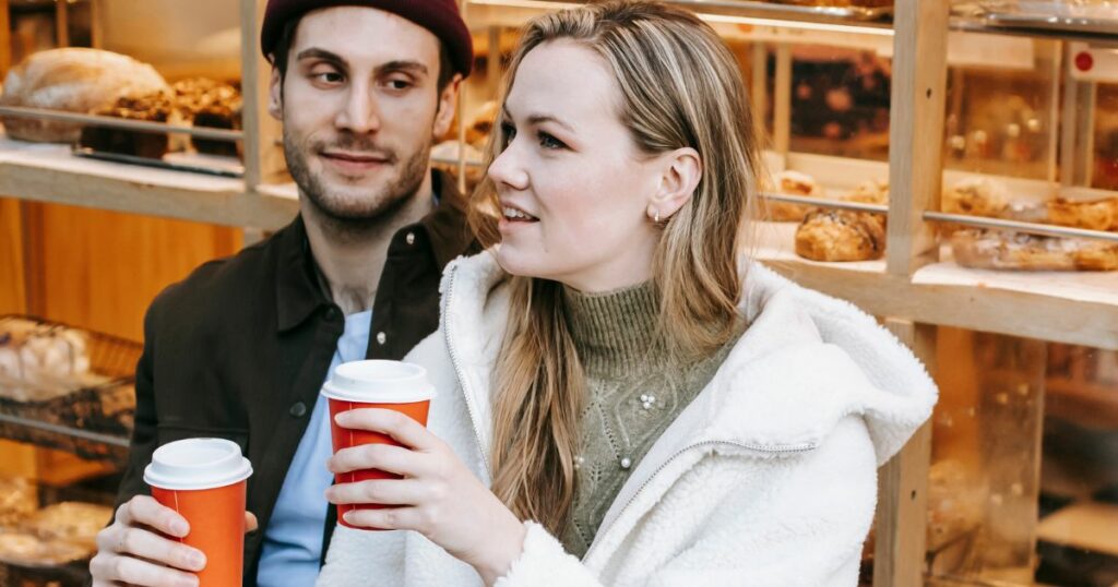 A man looking at a woman while drinking takeout coffee